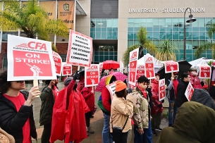 A photograph of demonstrators holding umbrellas and signs, one of which says "Faculty Working Conditions Are Student Learning Conditions” and others of which say “CFA On Strike!”