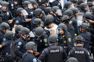 A single pro-Palestinian demonstrator is surrounded by dozens of police officers wearing helmets.